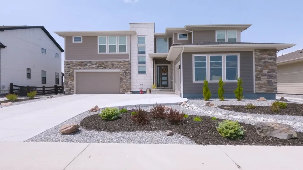 A sleek modern home with stacked windows, bright siding, and a spacious driveway. Landscaping includes rock mulch and small shrubs.